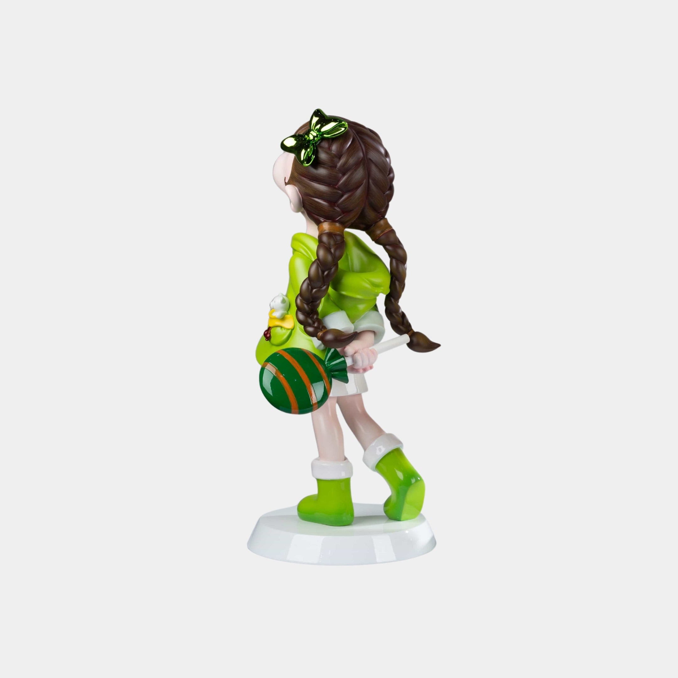 The Meadow Green Lulabelle Sculpture - 60cm by Giant Sculptures is a whimsical polyurethane art piece of a brown-haired girl in green attire, holding a green-orange ball, standing on a white base and facing away. Eco-friendly design.