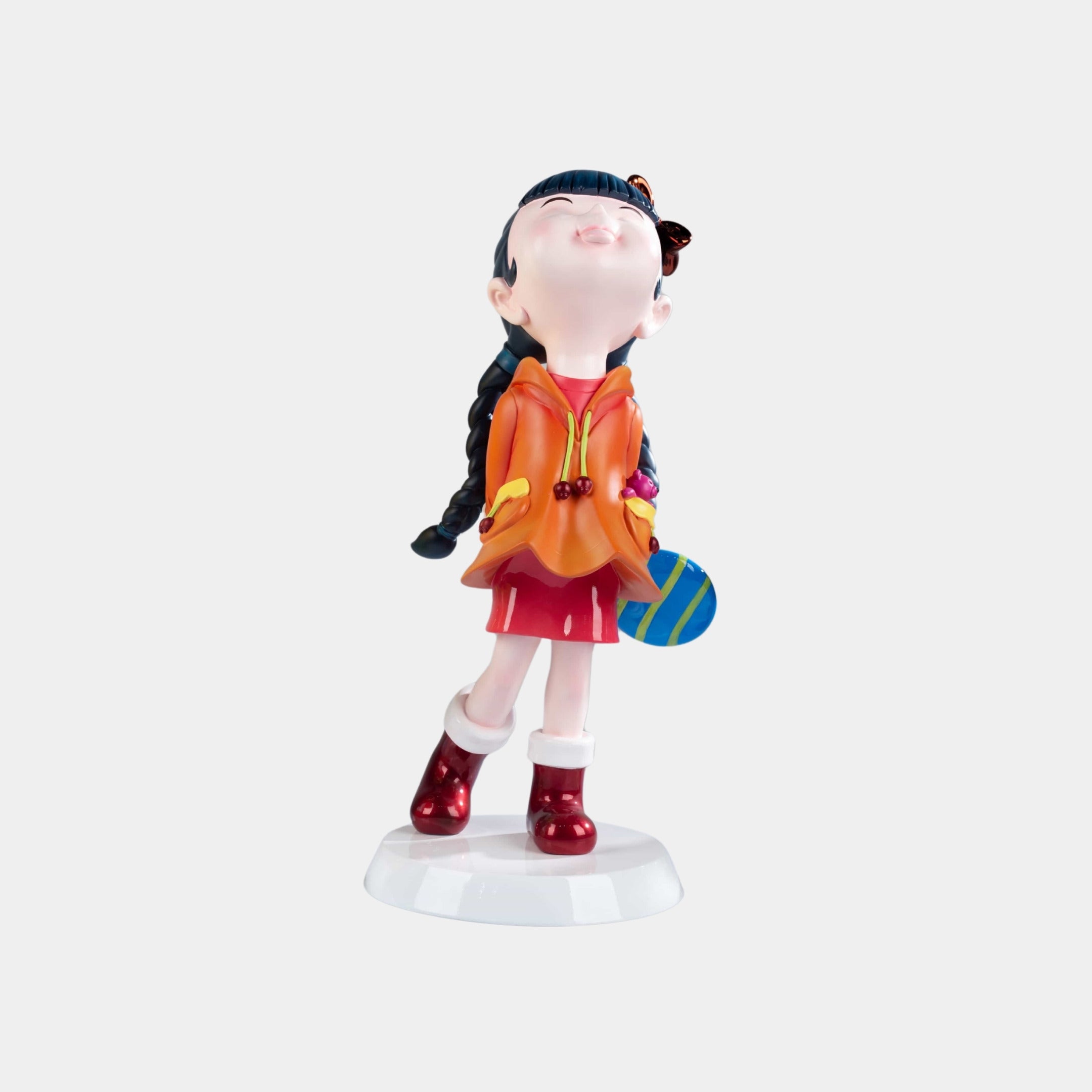 The Tangerine Orange Lulabelle Sculpture - 60cm by Giant Sculptures features a vibrant figurine of a girl with braided hair in a red skirt, orange jacket, and red boots on a white base—an expressive decorative statement piece.