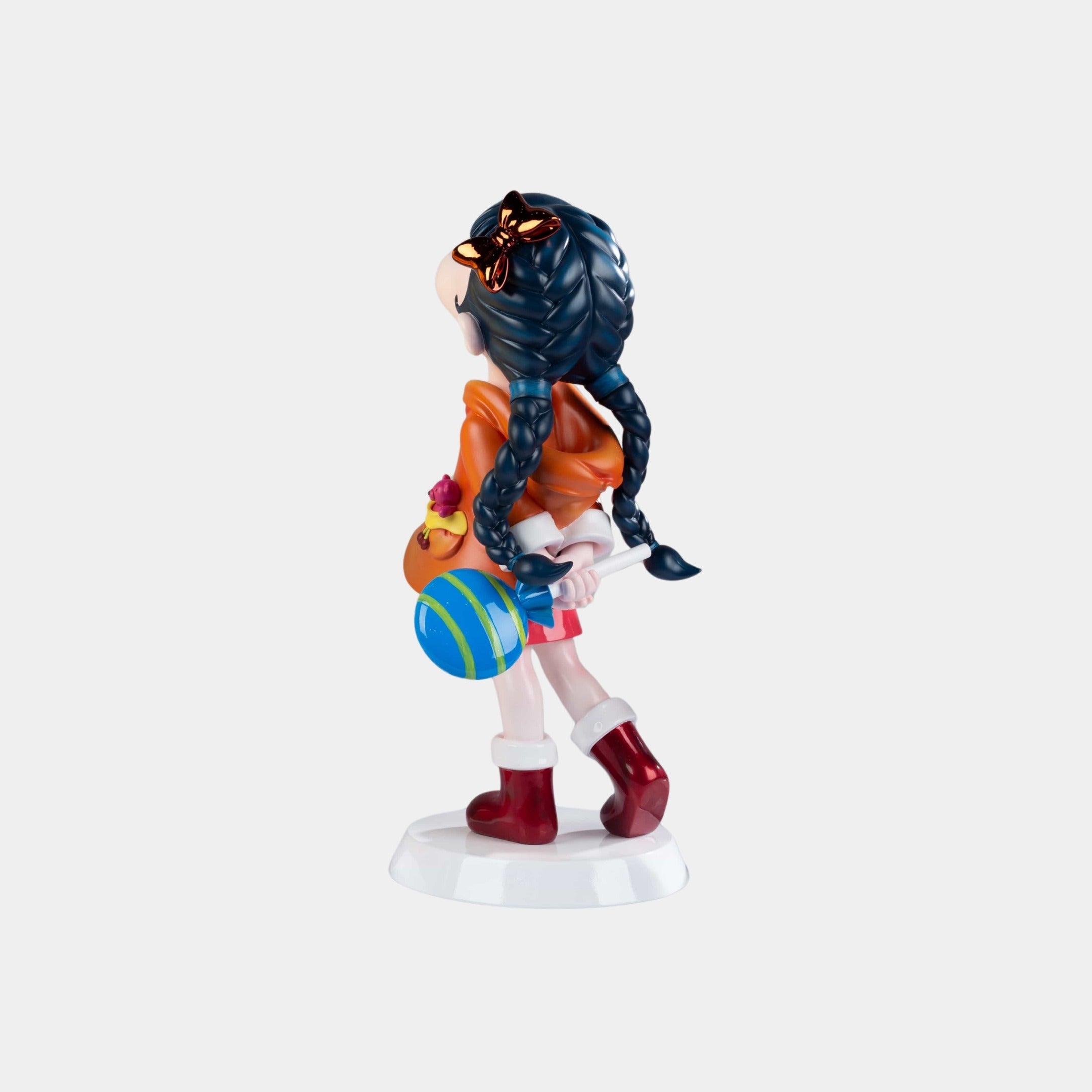 The Tangerine Orange Lulabelle Sculpture - 60cm by Giant Sculptures features a girl with long blue braids, orange top, red skirt, holding a colorful ball and pouch on a white base—perfect as a unique decorative statement.