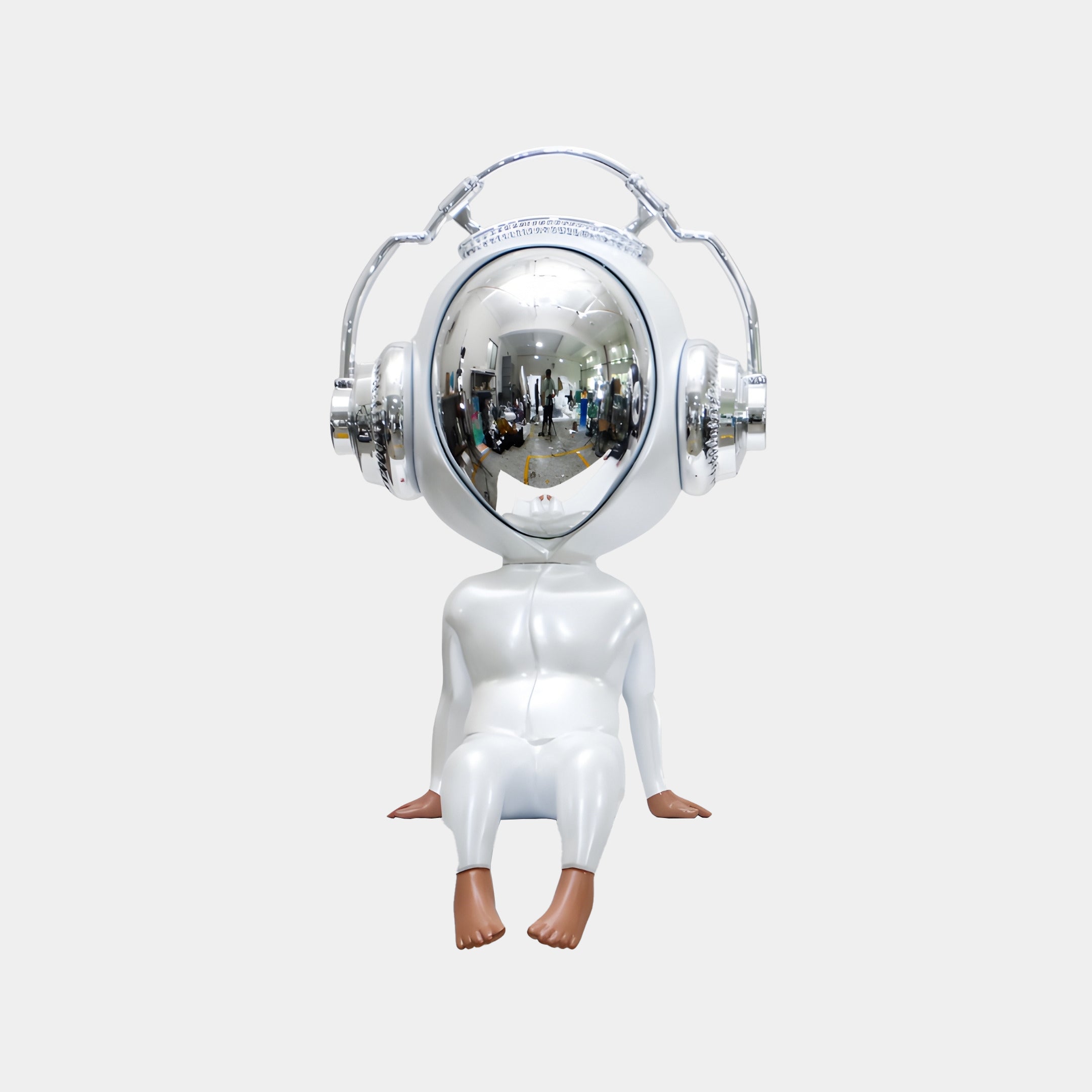The Giant Sculptures Arctic White Alien Beats Figure (55cm) features a shiny, futuristic doll with a large reflective helmet and oversized headphones, seated with brown hands and feet visible against a plain white background.