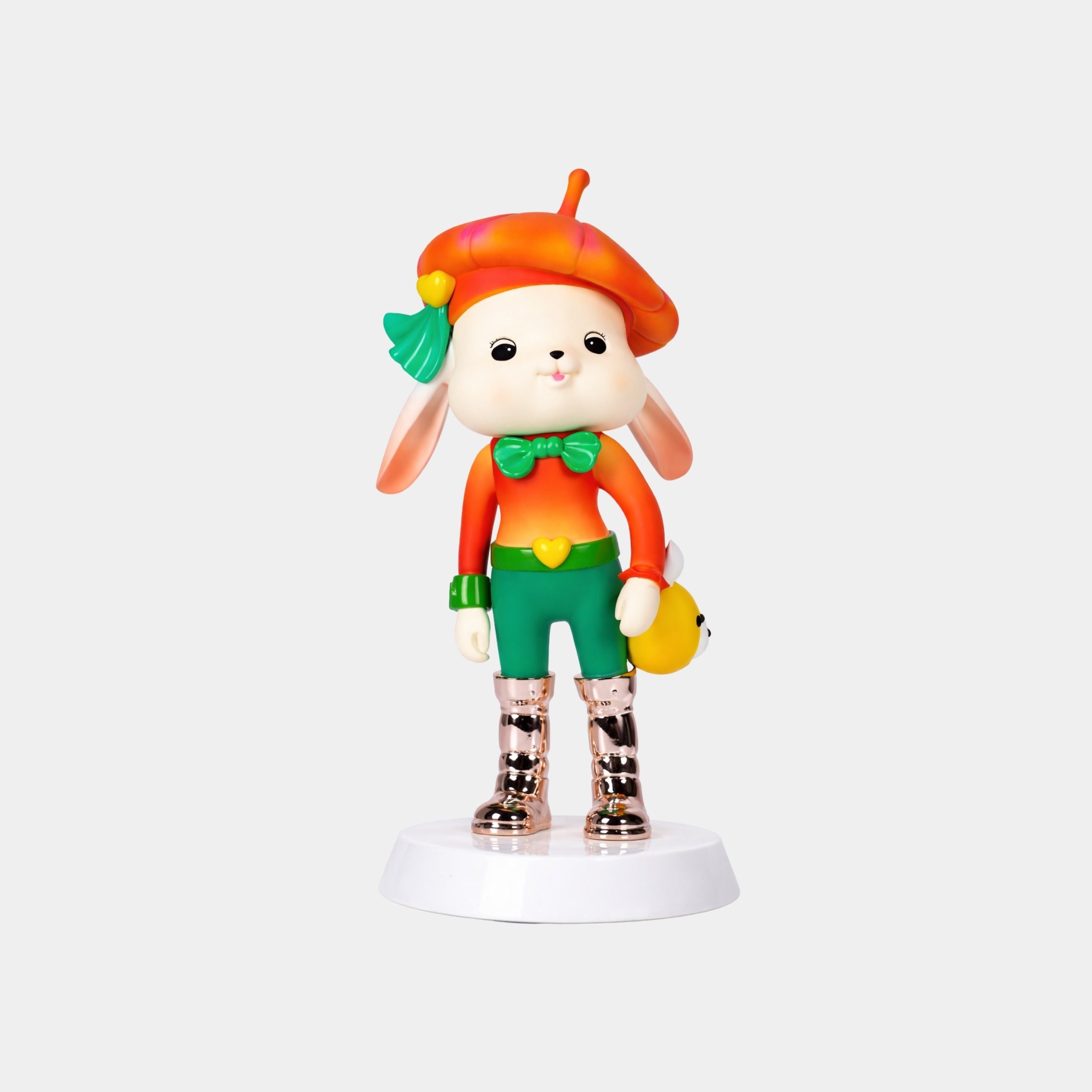 The Sunset Pop Bunny Figure - 58cm by Giant Sculptures is a designer vinyl art toy with an orange beret, green shorts, green bow tie, gold boots, holding a yellow animal and standing on a white display base.