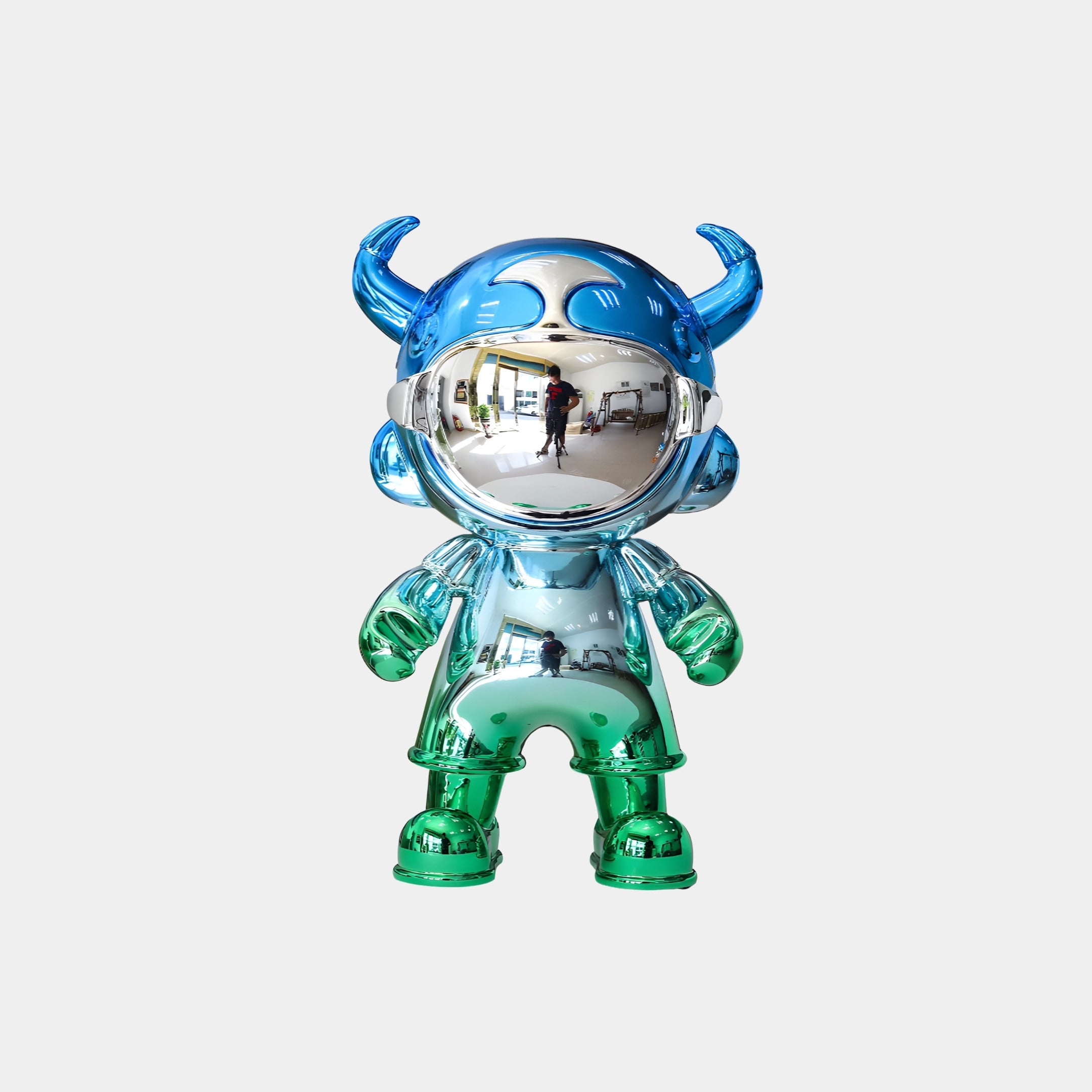 The Giant Sculptures Blue & Green Electroplated Astro Devil Figure (35cm) features blue horns, a helmet, green boots and gloves, and a reflective silver face that mirrors its surroundings.