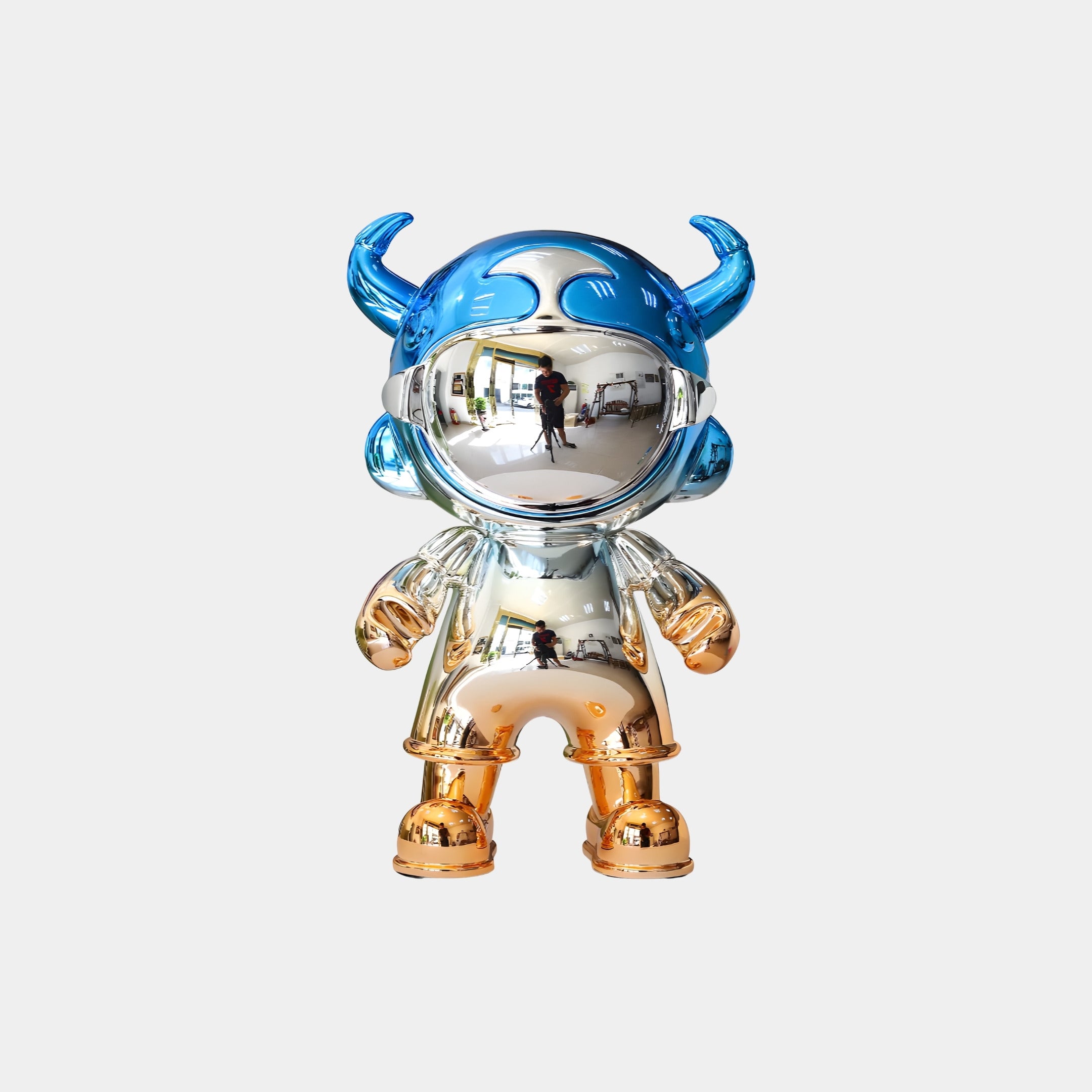 A shiny humanoid figure with a mirrored visor, blue horned helmet, and gold hands and boots stands on a plain background. The Blue & Copper Electroplated Astro Devil Figure - 35cm by Giant Sculptures shows visible human reflections.