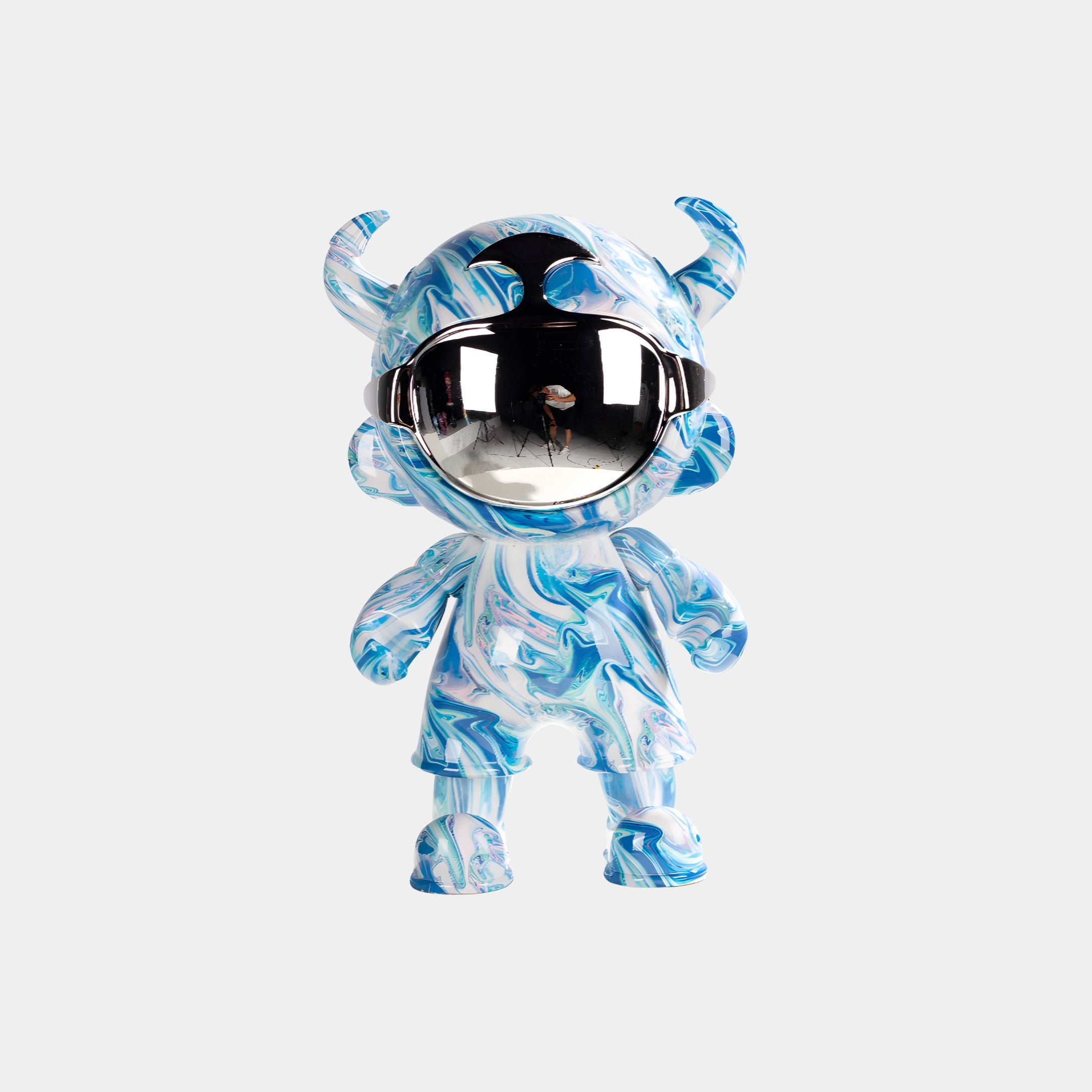 The Glacier Swirl Astro Devil Figure - 35cm by Giant Sculptures features blue and white marbling, small horns, and a mirrored faceplate reflecting a person and curved interior, set against a plain light gray background.