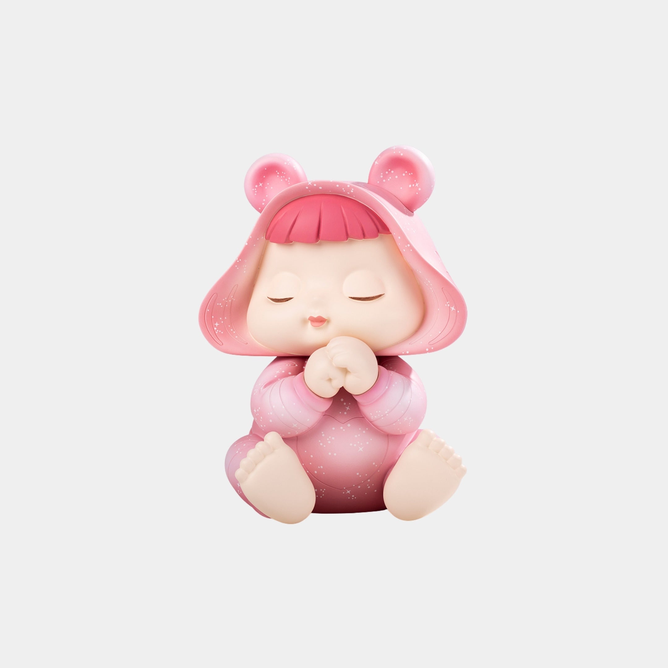 The Giant Sculptures Pink Stardust Baby Dreamer Figure (30cm) features a child with pink hair in a sparkly hooded bear outfit, eyes closed, sitting cross-legged with hands clasped on a plain white background.