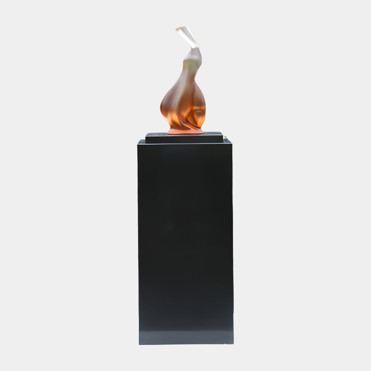 Amber to Clear Twisting Flame Resin Sculpture (182cm) by Giant Sculptures, a flame-like form fading to clear at its tip, set on a black marble block atop a tall black plinth against a plain white background.
