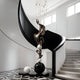 A modern curved staircase with black railing encircles the Giant Sculptures Balance Bronze Abstract Steel Sculpture (180cm), a piece of twisting forms and spheres, set on a geometric floor in a bright, white-walled room with large windows.