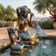 Classical Dual Mermaid Bronze Fountain by Giant Sculptures, two figures wringing water from their hair into a stone pond, set in a Mediterranean garden.