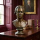 Classical Mozart Composer Bronze Bust by Giant Sculptures on a wooden desk in a burgundy-panelled study, with leather books, brass candlestick, and framed portrait.
