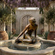 Classical Semi-Reclined Nude Female Bronze Fountain Sculpture by Giant Sculptures, set in a stone basin beneath a wisteria-draped pergola in a Mediterranean courtyard.