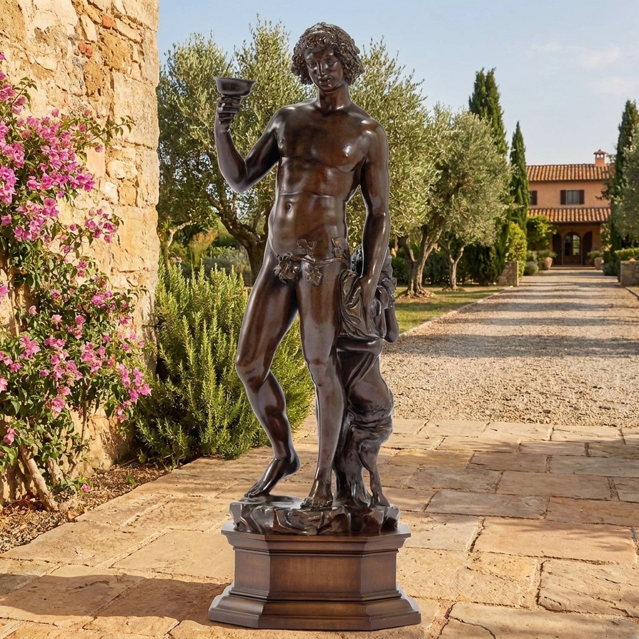 Classical Standing Bacchus Bronze Sculpture by Giant Sculptures on a stepped plinth in a Tuscan courtyard, raising a chalice beside bougainvillea and olive trees.