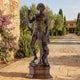 Classical Standing Bacchus Bronze Sculpture by Giant Sculptures on a stepped plinth in a Tuscan courtyard, raising a chalice beside bougainvillea and olive trees.