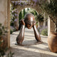 Giant Sculptures' 160cm Contemporary Blindfolded Emerging Head bronze stands on a stone courtyard beneath a wisteria-draped archway flanked by lavender and olive trees.