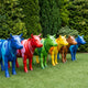 Row of Contemporary Life-Size Painted Cow Bronze Sculptures by Giant Sculptures in blue, red, green, yellow and brown high-gloss finishes on a lawn.