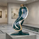 Contemporary Melting Clock Bronze Sculpture by Giant Sculptures, 70cm teal and gold patina piece displayed on a concrete plinth beside a reflecting pool in a gallery.