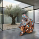 Contemporary Mosaic Figure Bronze Sculpture 150cm by Giant Sculptures, seated figure with hexagonal cells in brown, black, white, coral, and turquoise, beside an olive tree courtyard.