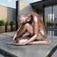 Giant Sculptures 140cm Contemporary Seated Nude Female Figure Bronze Sculpture in folded pose with warm reddish-brown patina, on a paved terrace beside a reflecting pool.