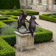 Contemporary Sparring Rabbits Bronze Sculpture by Giant Sculptures, two upright hares with dark patina on a stone plinth in a formal boxwood garden.