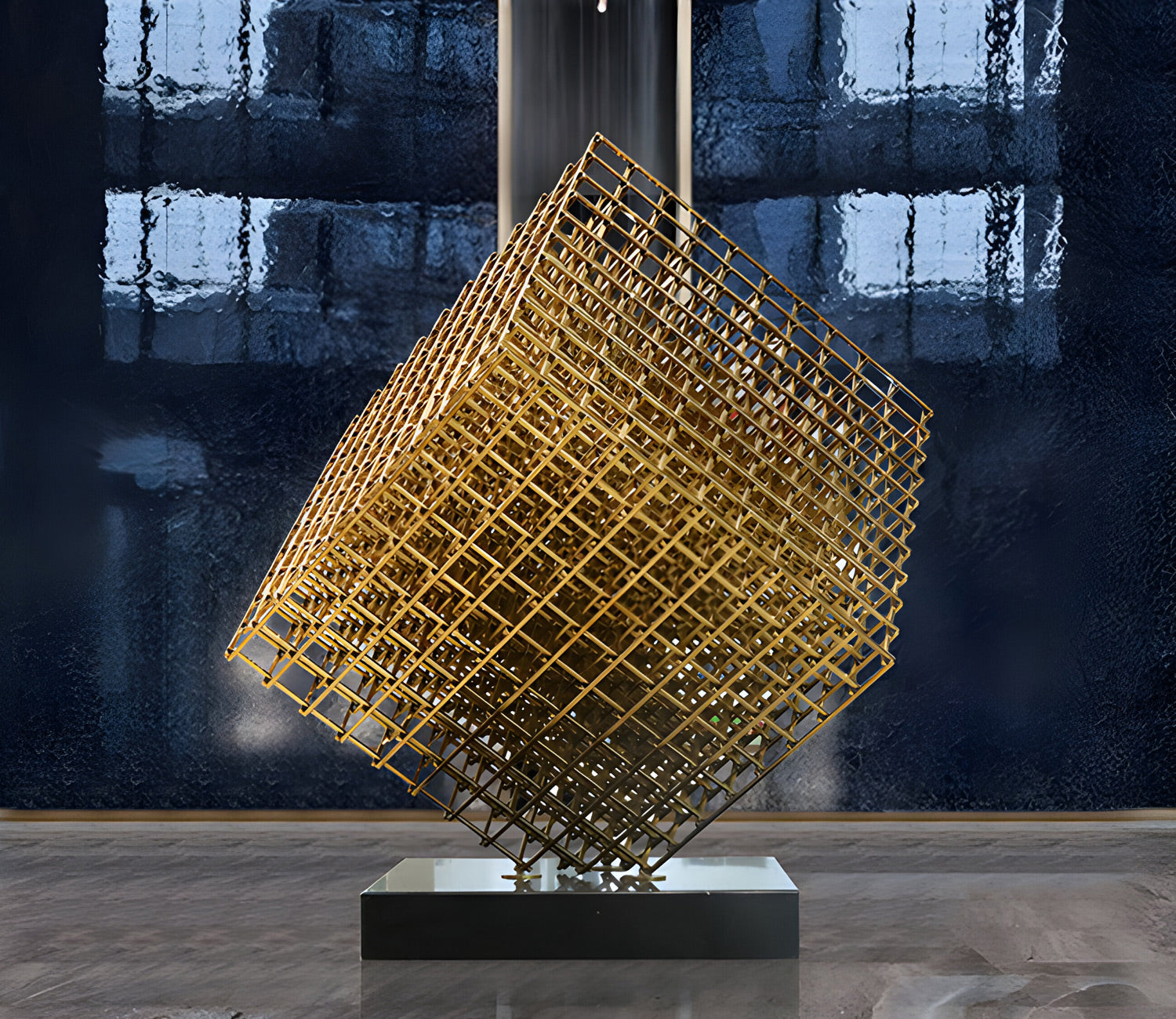 Gold geometric cube sculpture made of intersecting metal bars, positioned on a black base in the center of a modern interior with stone walls and reflective marble flooring.