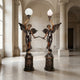 Large Classical Angel Torchiere Floor Lamp Bronze Sculpture by Giant Sculptures, a 240cm winged pair on plinths holding globe and flame lights in a marble hall.