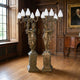 Pair of Large Classical Candelabra Figure Bronze Sculptures by Giant Sculptures, draped females holding five-arm candelabra with frosted flame shades, in a wood-paneled hall.
