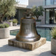 Large Classical Church Bell Bronze Sculpture by Giant Sculptures on a stone slab beside a pool, with olive trees, lavender planters, and concrete architecture.