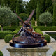 Large Classical Cupid and Psyche Bronze Sculpture by Giant Sculptures on a dark oval plinth atop a stone pedestal in a formal hedged garden.