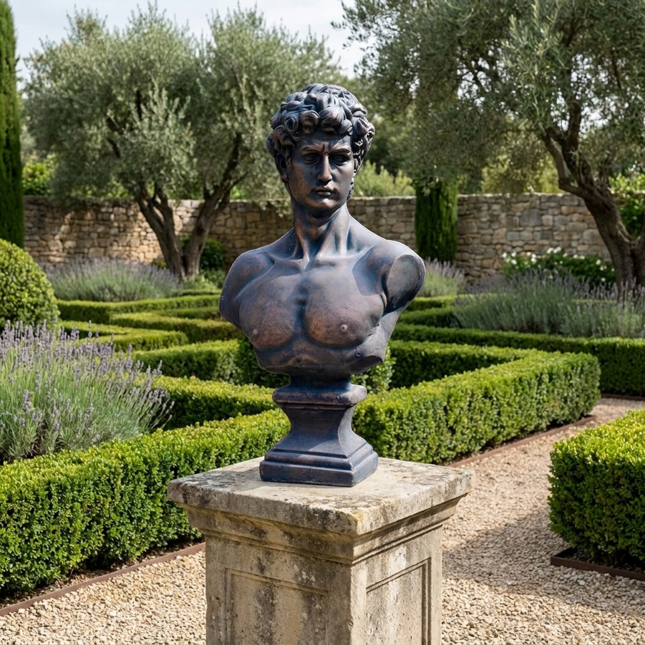 Giant Sculptures Large Classical David Bust in dark bronze on a stone plinth, displayed in a formal garden with boxwood hedges, lavender, and olive trees.
