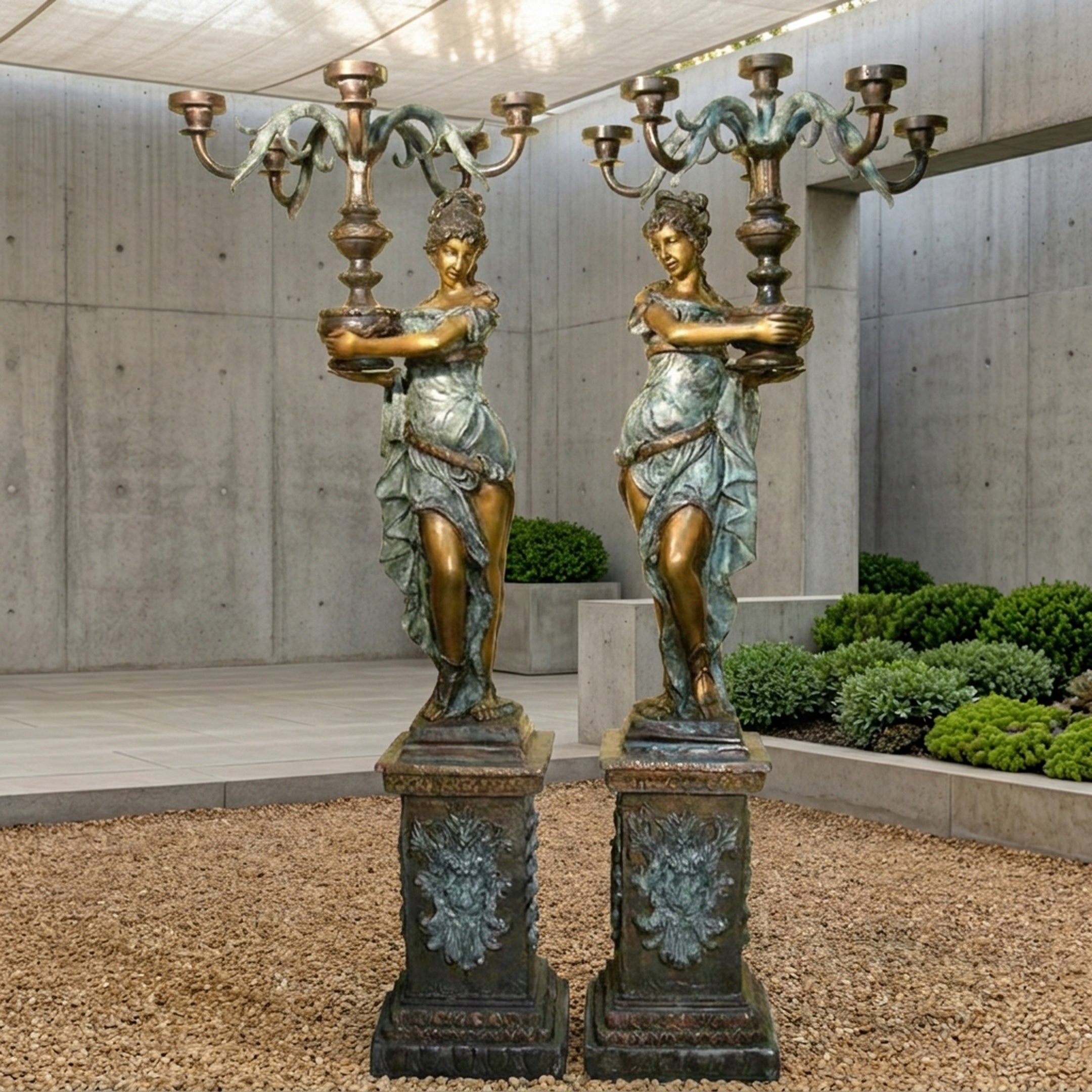 Pair of Giant Sculptures Large Classical Draped Goddess Candelabra Bronze Sculptures in verdigris and gold finish, displayed on ornate pedestals in a concrete courtyard.
