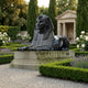 Large Classical Egyptian Sphinx Bronze Sculpture by Giant Sculptures, 180cm recumbent figure with dark patina on a stone plinth in a formal hedged garden.