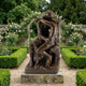 Large Classical Embracing Figures Bronze Sculpture by Giant Sculptures, 180cm, on a stone plinth in a formal rose garden with boxwood hedges and arch.
