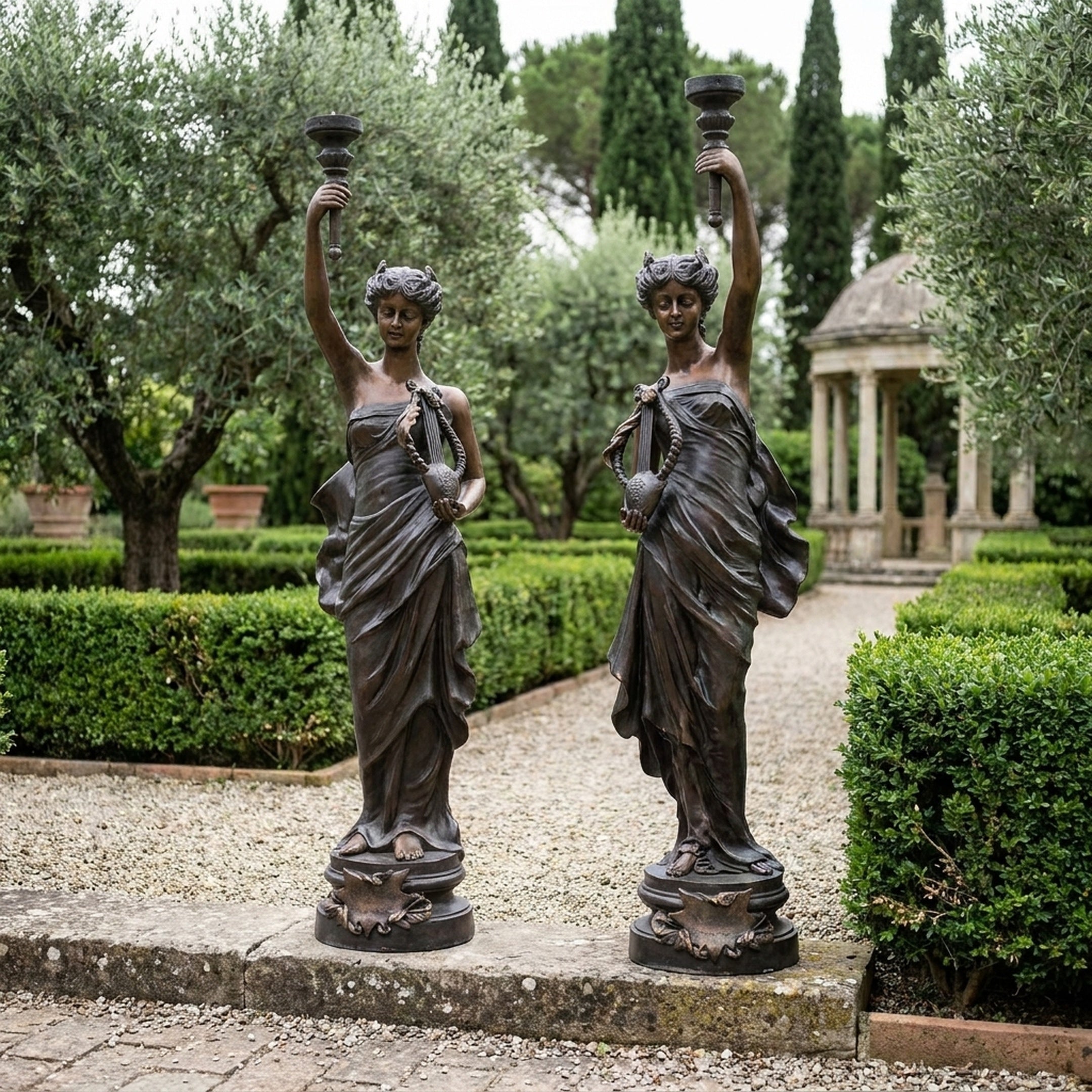 Large Classical Goddess Pair Bronze Sculpture by Giant Sculptures, 180cm draped female figures raising candelabra torchères, displayed on a formal garden path.