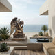 Large Classical Kneeling Angel Bronze Sculpture by Giant Sculptures with golden patina, head bowed into hand and wings raised, on a terrace overlooking the sea.