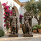 Large Classical Roman Warrior Pair Bronze Sculpture by Giant Sculptures displayed in a Mediterranean courtyard with bougainvillea, olive tree, and arched white walls.