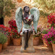Large Classical Seated Angel Bronze Sculpture by Giant Sculptures with two-tone verdigris wings, seated on a stone plinth among potted bougainvillea and olive trees.