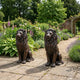 Large Classical Seated Lion Pair Bronze Sculpture by Giant Sculptures displayed on a stone patio beside a flowering English garden with lavender borders.