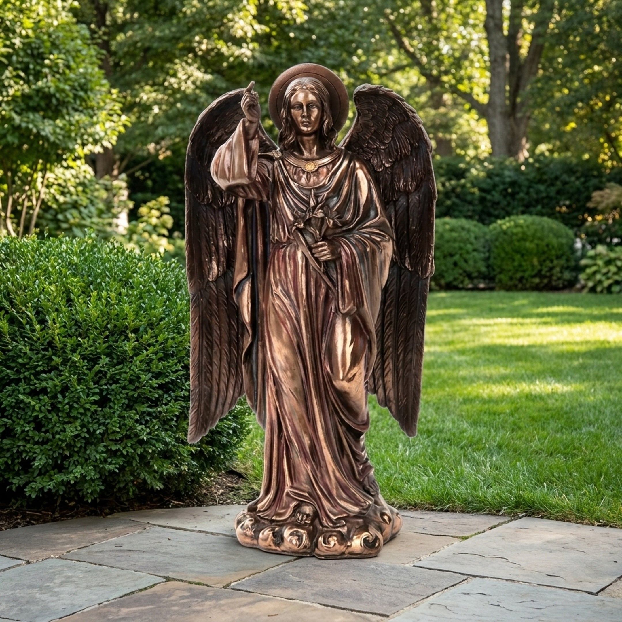 Large Classical Standing Angel Bronze Sculpture by Giant Sculptures with wings spread and finger raised skyward, displayed on a garden patio beside hedging.