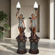 Pair of Giant Sculptures Large Classical Winged Figure Torch Lamp Bronze Sculptures on fluted pedestals, holding frosted flame shades aloft, in a stone alcove.