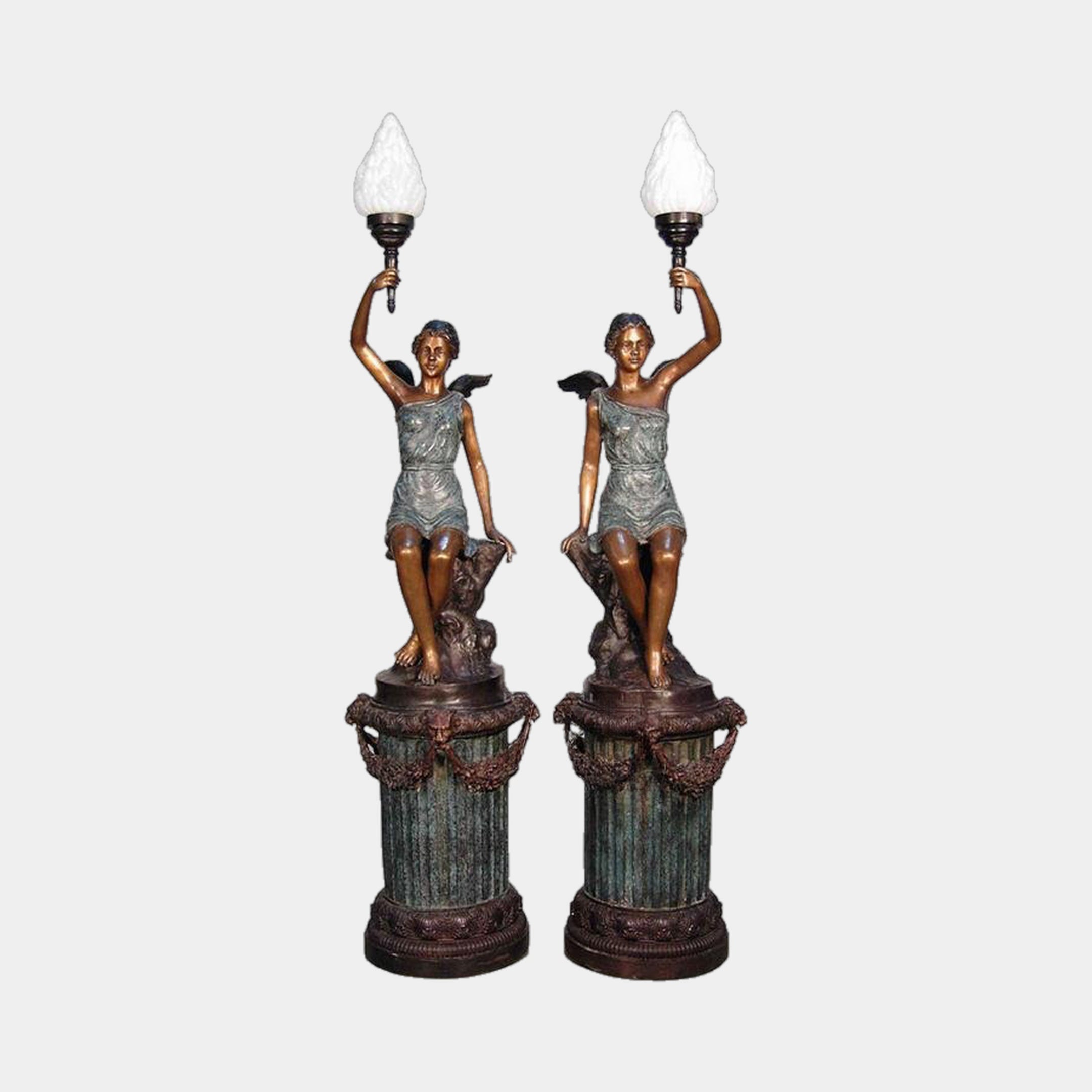 Mirrored pair of Large Classical Winged Figure Torch Lamp Bronze Sculptures by Giant Sculptures, seated robed figures raising frosted flame shades atop fluted columns.