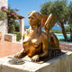 Large Classical Winged Sphinx Bronze Sculpture by Giant Sculptures in golden-amber finish, reclining on a stone plinth beside a pool with sea views.