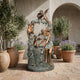 Giant Sculptures' Large Classical Woman and Cherubs Bronze Fountain 150cm with verdigris base in a Mediterranean courtyard framed by olive trees and lavender pots.