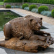 Giant Sculptures Large Contemporary Bear with Fish Bronze Sculpture in warm brown patina, crouched over a fish on a rocky base beside a garden pond.