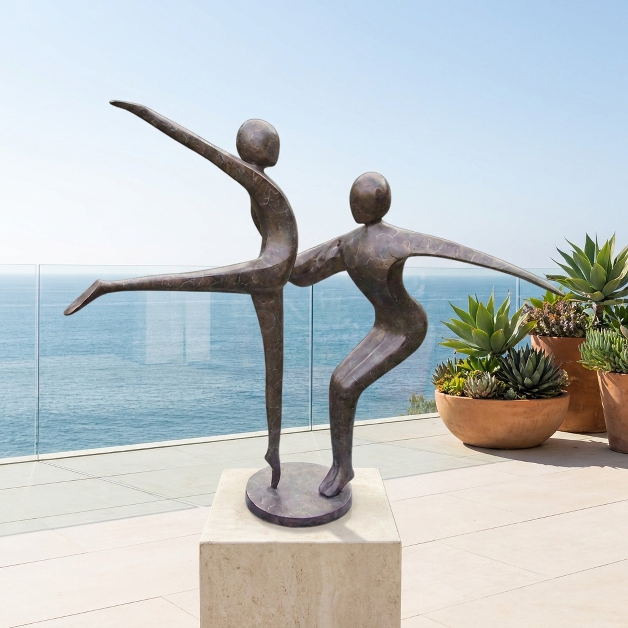 Large Contemporary Dancing Figures Bronze Sculpture by Giant Sculptures on a pale stone plinth, displayed on an oceanview terrace beside potted succulents.