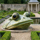 Large Contemporary Emerging Frog Head Bronze Sculpture by Giant Sculptures on a stone disc in a formal garden with lavender, hedges and pond.