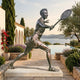 Large Contemporary Female Tennis Player Bronze Sculpture by Giant Sculptures, 210cm, mid-lunge follow-through on a stone plinth beside a poolside terrace.