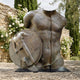 Large Contemporary Fragmentary Warrior Torso Bronze Sculpture by Giant Sculptures, displayed outdoors on stone paving beside white roses and cypress trees.