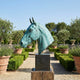 Large Contemporary Horse Head Bronze Sculpture by Giant Sculptures in verdigris patina on a dark plinth, set in a formal garden with lavender and olive trees.