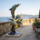 Large Contemporary Leaping Dolphin and Reef Bronze Sculpture by Giant Sculptures on a seaside terrace with stone balustrade and coastal view.