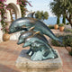 Giant Sculptures Large Contemporary Leaping Dolphins Bronze Sculpture with verdigris patina on a stone plinth, displayed on a Mediterranean terrace overlooking the sea.