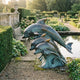 Large Contemporary Leaping Dolphins Bronze Sculpture by Giant Sculptures, three dolphins rising from a wave base in verdigris patina beside a formal garden pond.